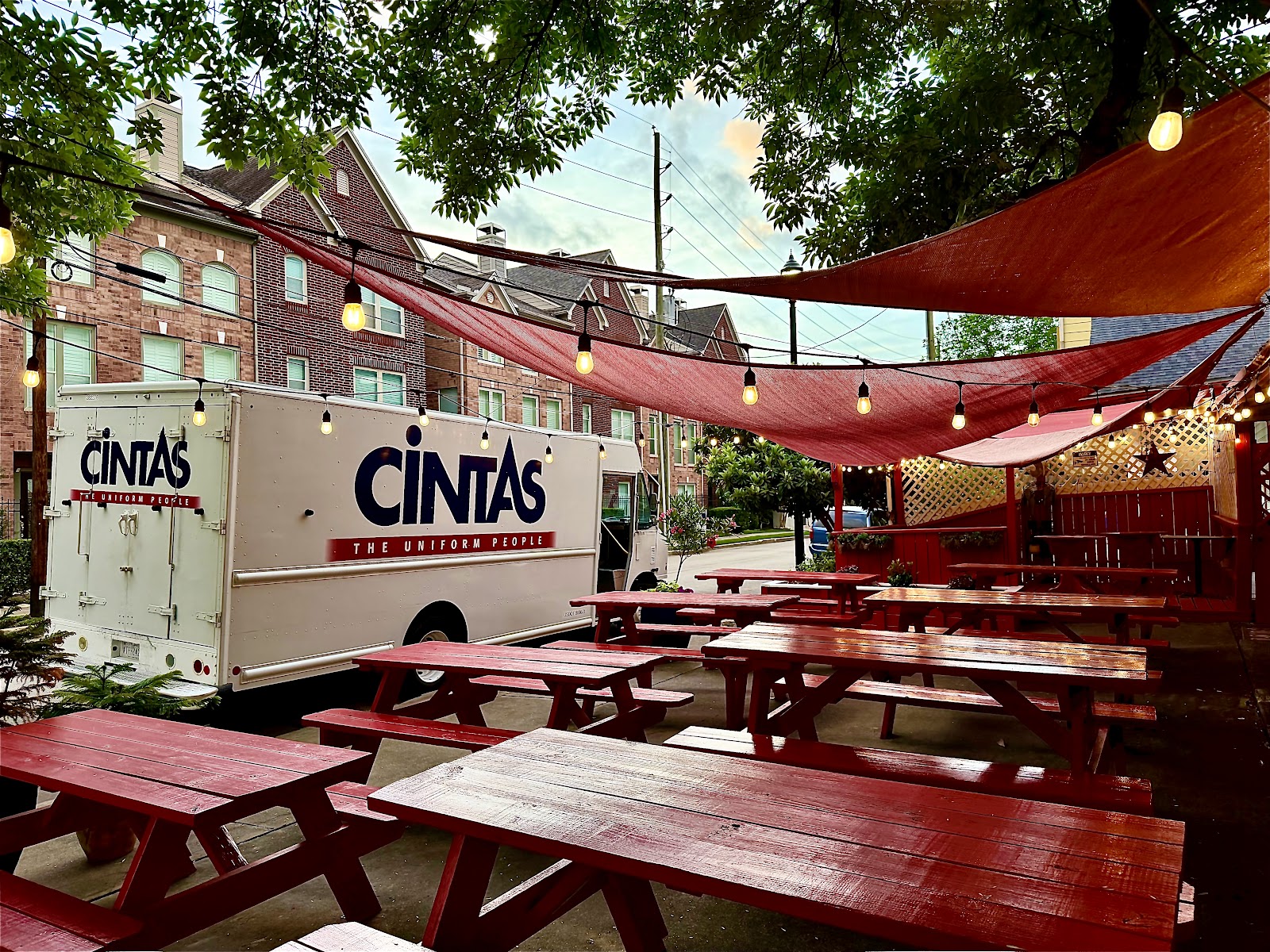 Red-topped picnic tables under a shade sail, beside brick and garden lighting
